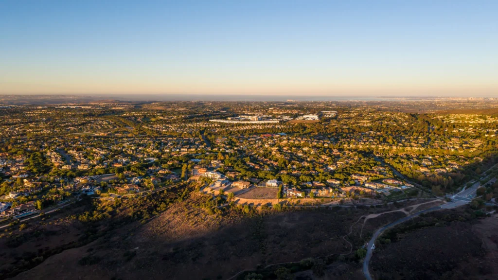 Aerial view of a sprawling suburban city at sunset, with houses, streets, and green trees.