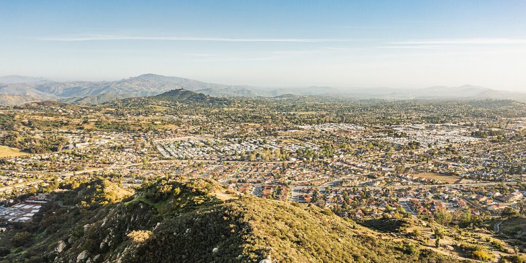Aerial view of a sprawling suburban valley with dense housing, rolling hills in the foreground and distant mountains on the horizon.